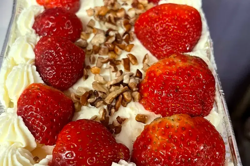 Cake topped with whipped cream, strawberries and pecans